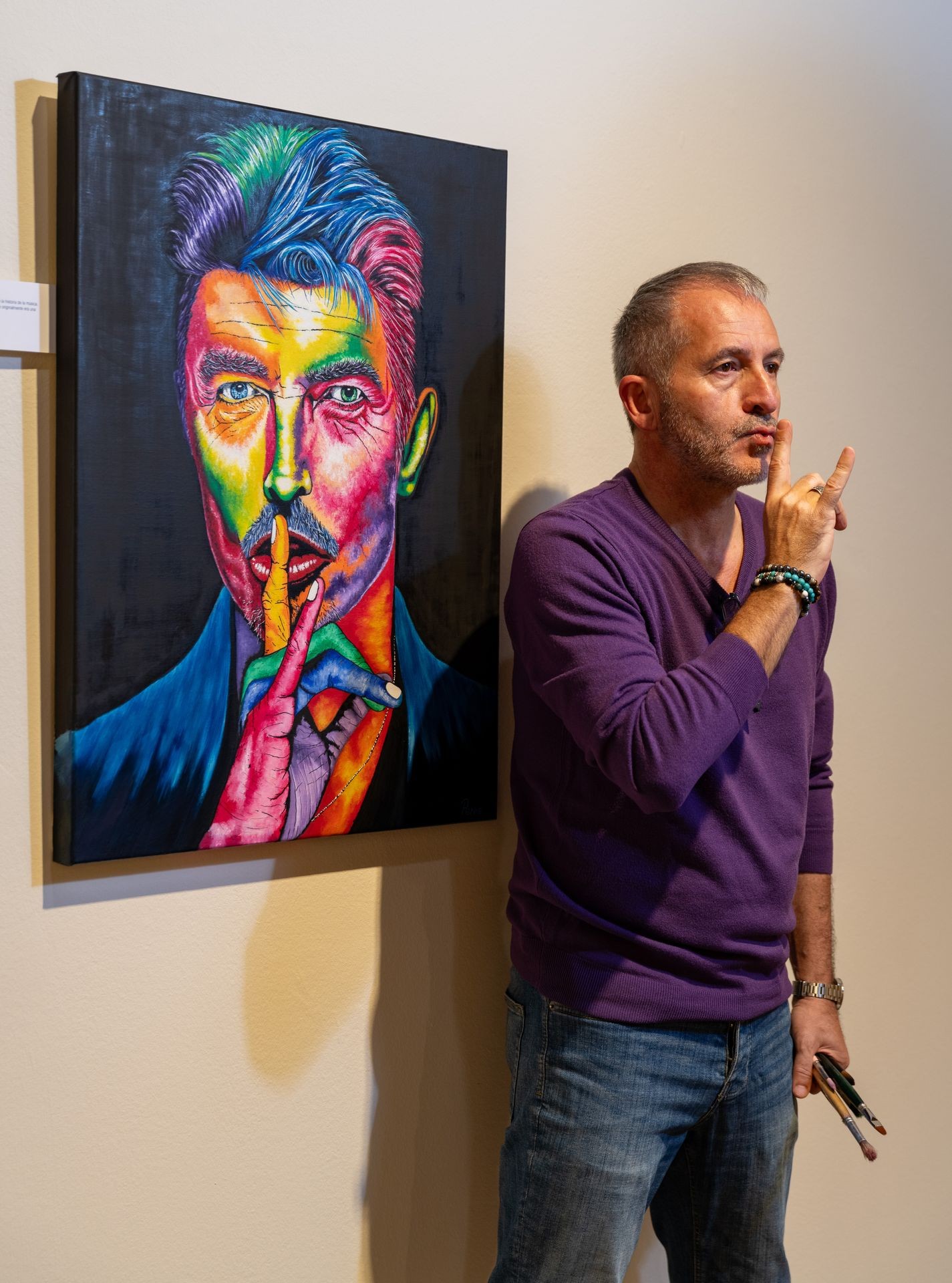 Man in purple shirt mimicking a colorful portrait of a person holding finger over lips.
