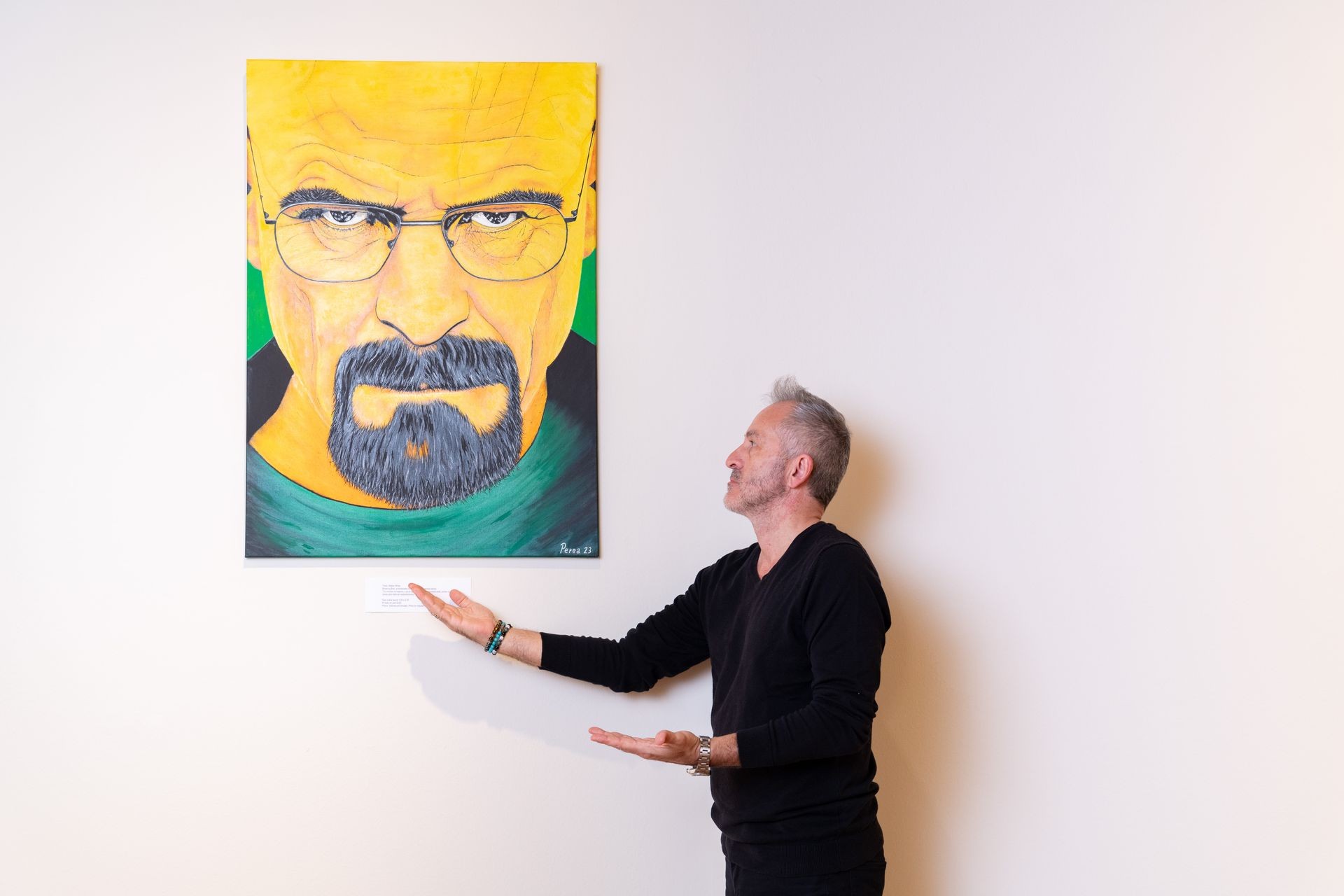 Man gesturing toward a vibrant portrait painting on a white wall.