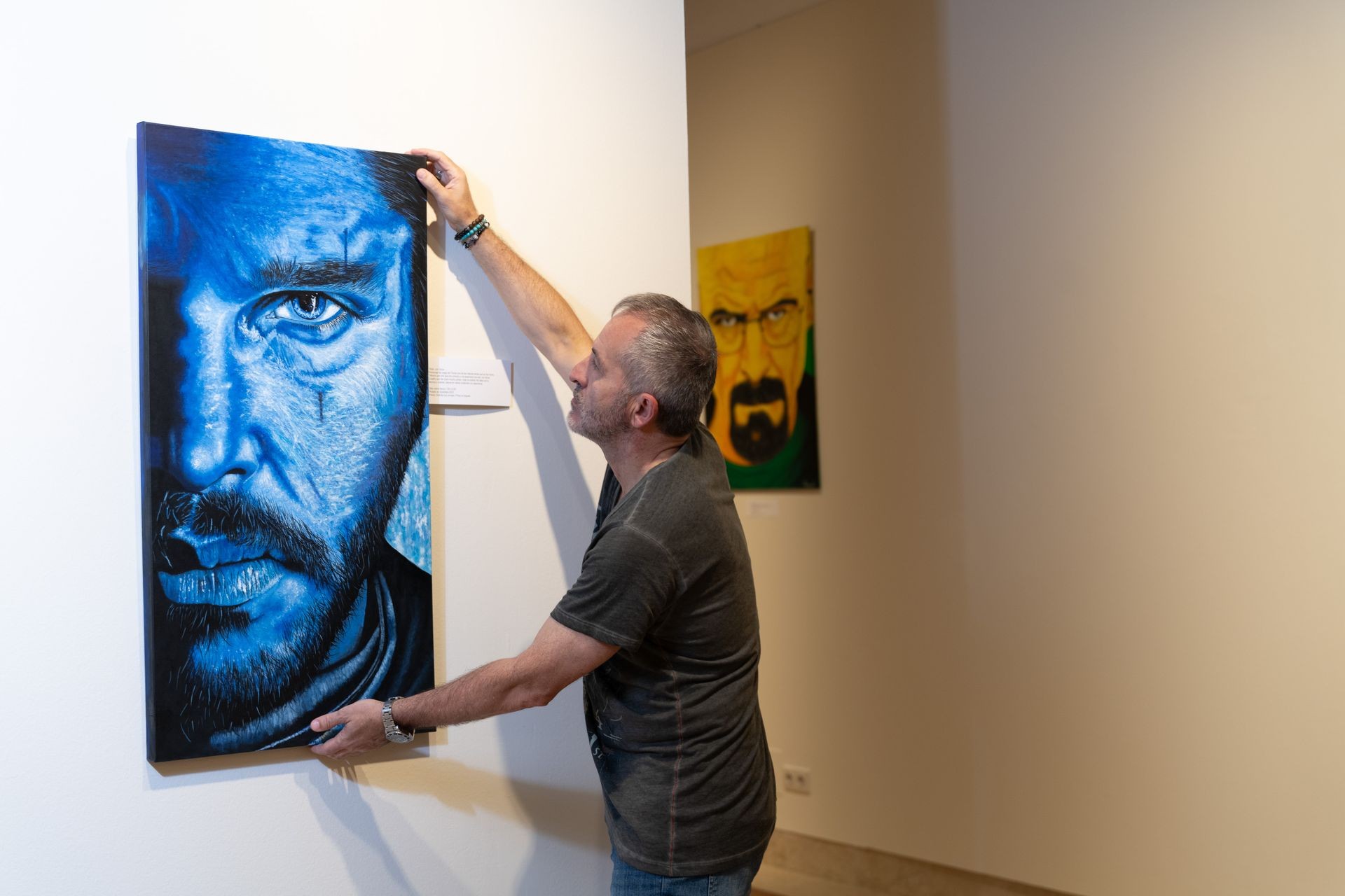 Person hanging a blue-toned portrait painting on a gallery wall.